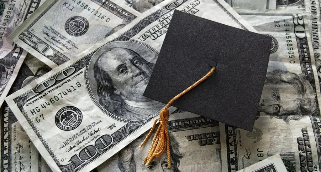 Graduation cap on top of pile of money to represent tuition collection.