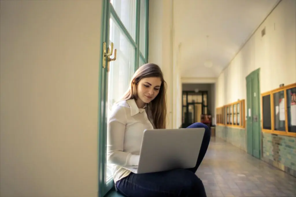 College student managing tuition collection online while sitting in a university hallway with a laptop.
