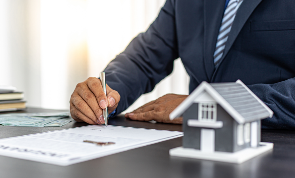 Landord in suit writing on collection agency document, with small house on desk.