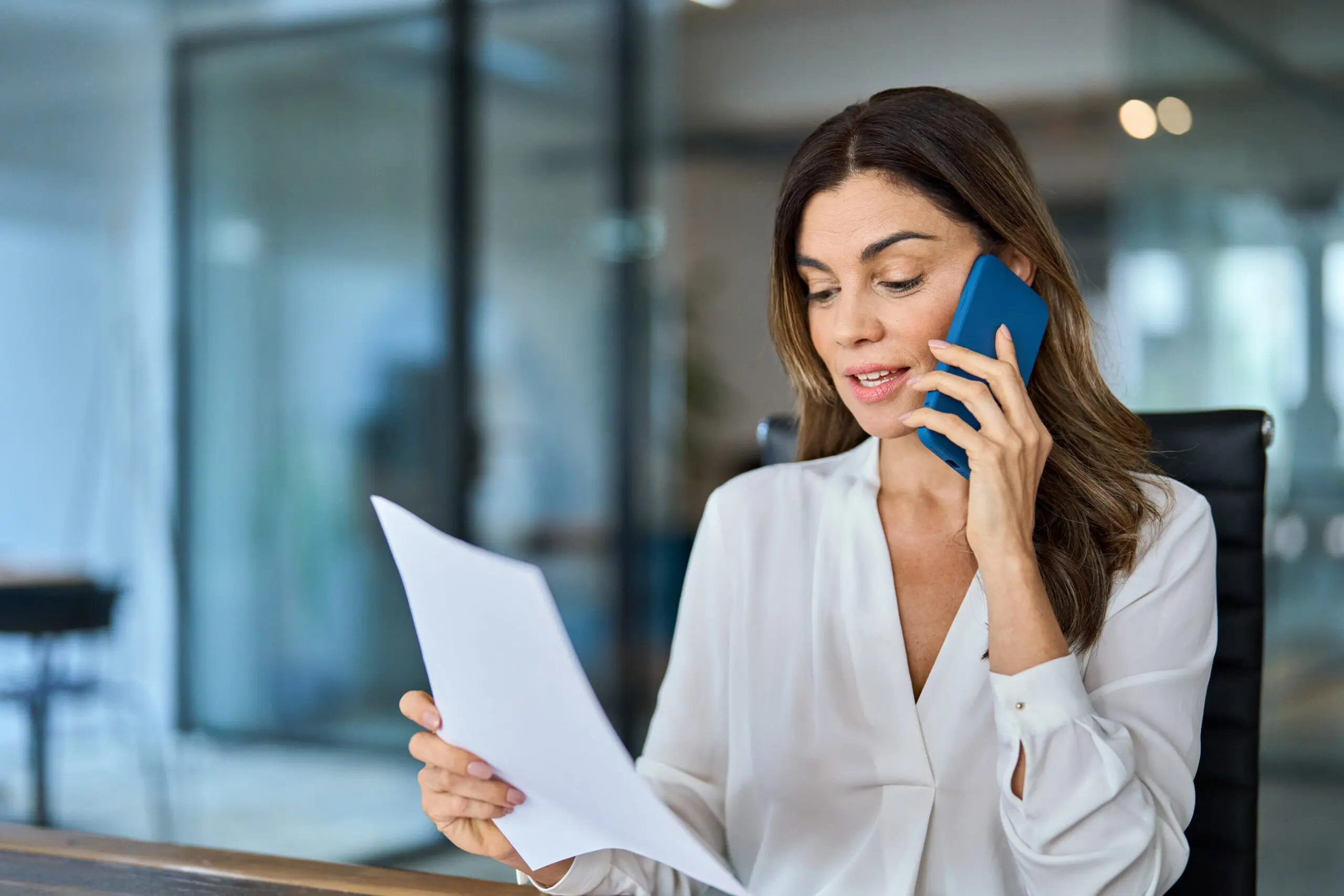 Collection company employee reviewing a document while speaking on the phone at a desk