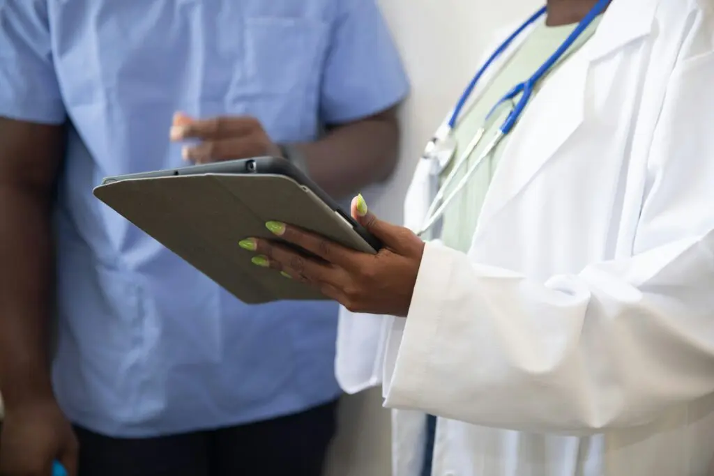 patients collections process - Collection Recovery Services Doctor with lab coat and stethoscope showing nurse a tablet, discussing the patient collections process.