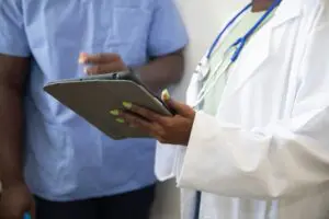 Doctor with lab coat and stethoscope showing nurse a tablet, discussing the patient collections process.