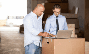 Small business owner reviewing strategy with a b2b collection agency employee on a laptop in a warehouse.