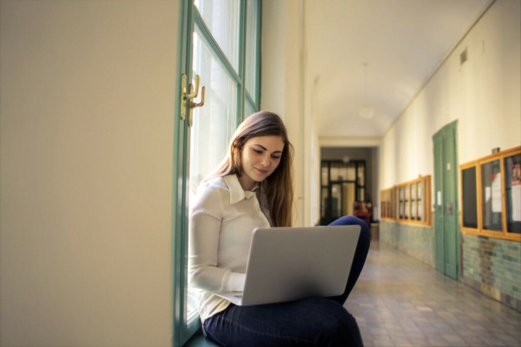 College student managing tuition collection online while sitting in a university hallway with a laptop.