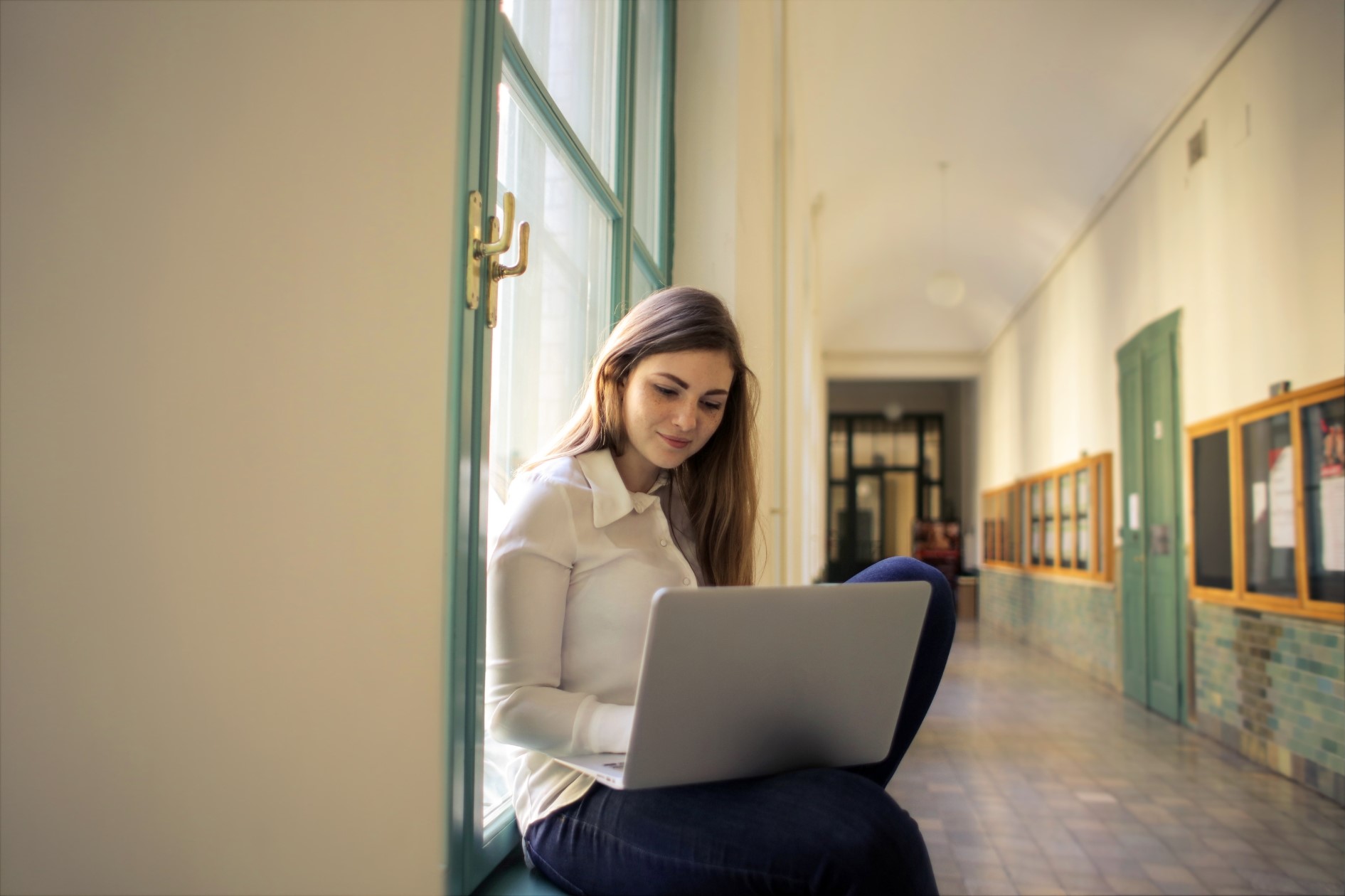 College student managing tuition collection online while sitting in a university hallway with a laptop.