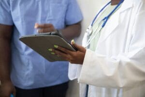 Doctor with lab coat and stethoscope showing nurse a tablet, discussing the patient collections process.