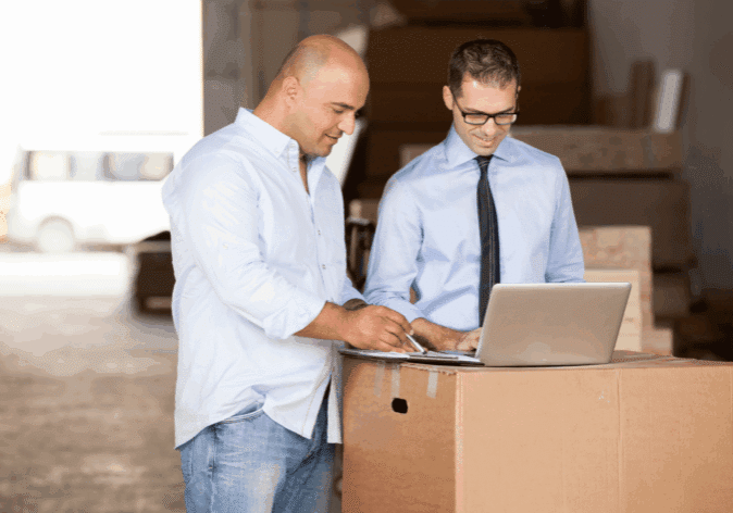 Small business owner reviewing strategy with a b2b collection agency employee on a laptop in a warehouse.