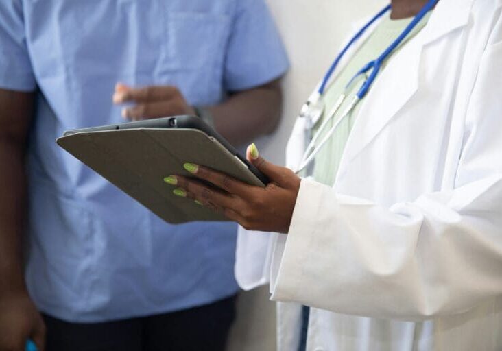 Doctor with lab coat and stethoscope showing nurse a tablet, discussing the patient collections process.