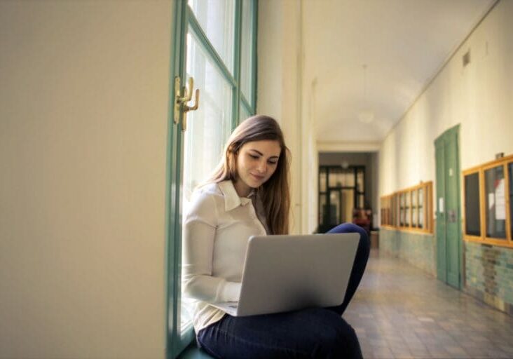 College student managing tuition collection online while sitting in a university hallway with a laptop.
